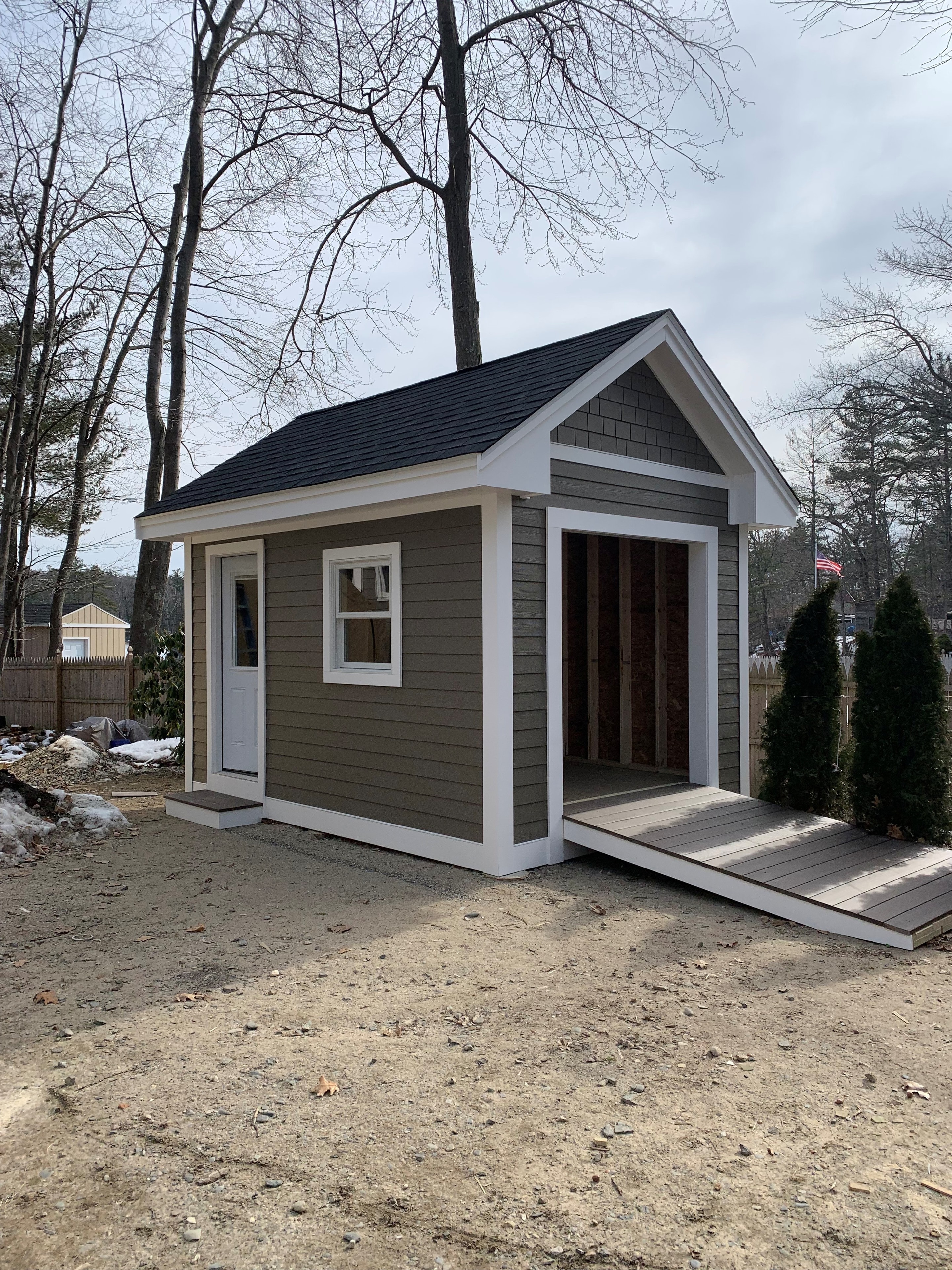 Custom shed with gray siding, white trim, and composite ramp